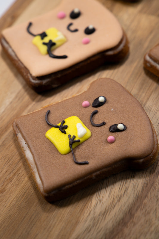 Decorative cookies shaped like a toast with a smiley face on a wooden surface