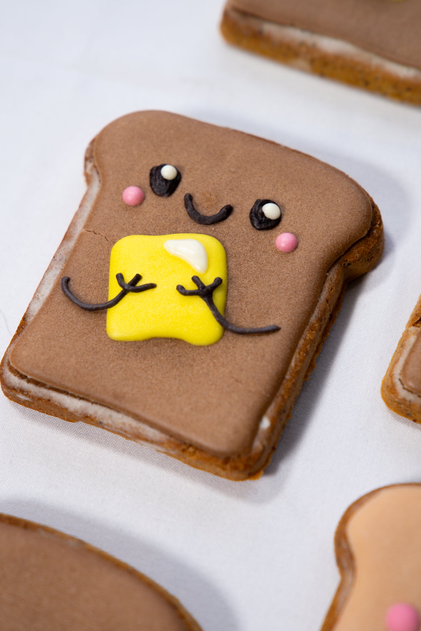Cookie shaped like a piece of toast with a face made from yellow fondant and pink candies on a white background.
